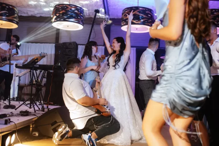 A bride in a white dress dances with guests while a Boston Band provides unforgettable wedding music at an indoor reception.