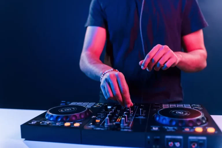 A person using a DJ controller with both hands, adjusting knobs and switches under blue and pink lighting, sets the perfect vibe for wedding music or a lively Boston band performance.
